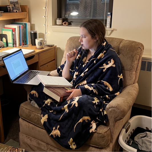 person sitting in a chair doing homework while wrapped in a black blanket with a crested gecko pattern