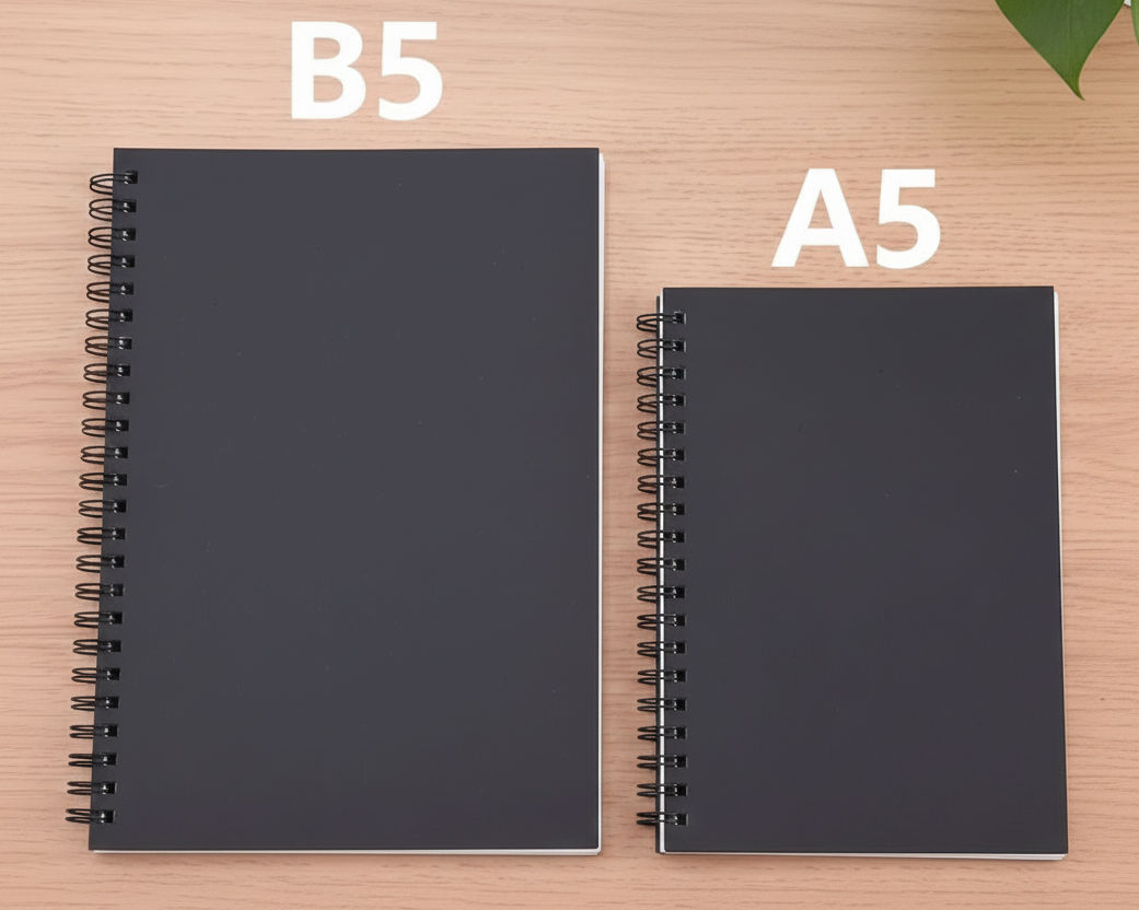 Two spiral-bound notebooks on a light wood desk, labeled B5 (176x250mm) and A5 (148x210mm). The notebooks are black with white binding.