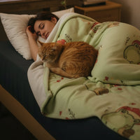 a light sage green blanket featuring a repeating cartoon pattern of a green frog wearing a red mushroom cap and snail.
