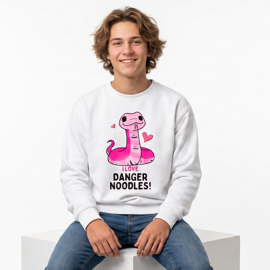 A young man with curly brown hair sits on a white block, wearing a white crewneck sweatshirt with a pink cartoon snake graphic and the text 'DANGER NOODLES!' on the front, paired with blue jeans against a plain white background.
