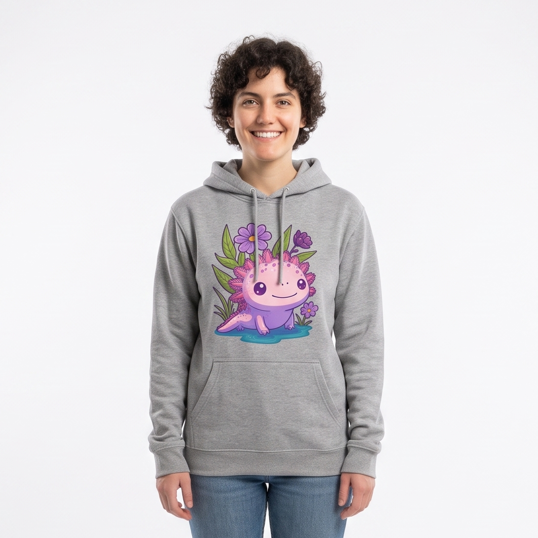 A person standing in a white studio wearing a heather gray pullover hoodie with a colorful cartoon axolotl graphic on the chest, blue jeans, and white sneakers. Softbox lights are visible on both sides of the backdrop.