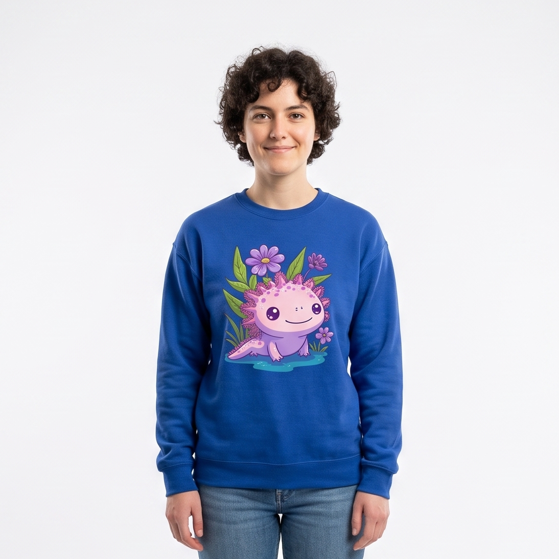 A person standing in a white studio setting wearing a royal blue crewneck sweatshirt with a colorful cartoon axolotl graphic on the front, paired with blue jeans and white sneakers.