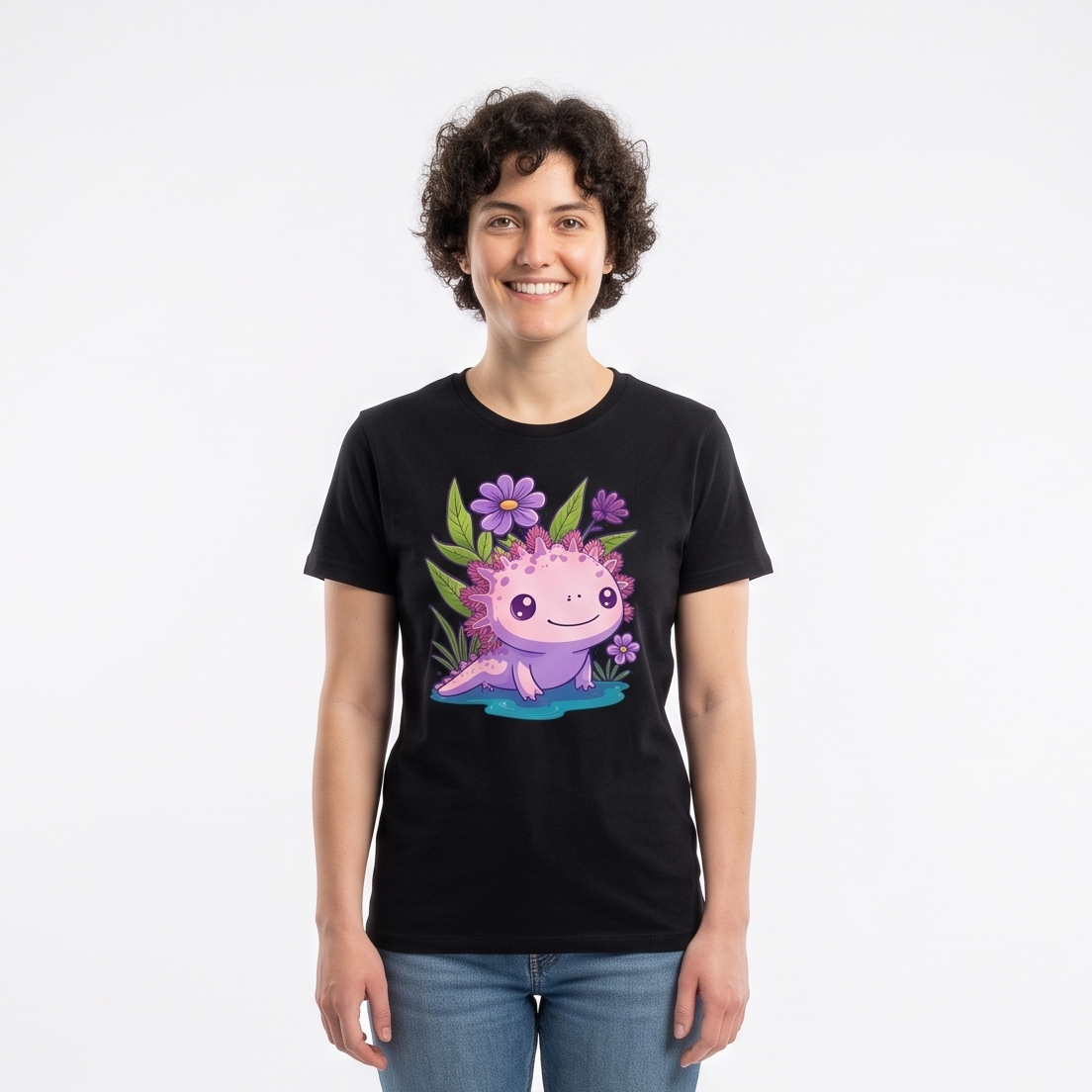 A person standing in a white studio wearing a black graphic T-shirt with a colorful cartoon axolotl design, blue jeans, and white sneakers. Softbox lights are visible on both sides of the backdrop.