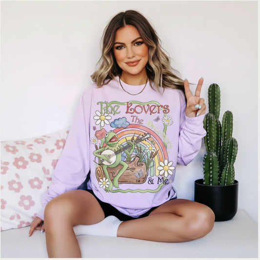 Person wearing a purple sweatshirt with a colorful graphic design featuring kermit, flowers, and a rainbow.