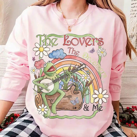 Person wearing a pink sweatshirt with a colorful graphic of a frog playing a banjo, flowers, and a rainbow.