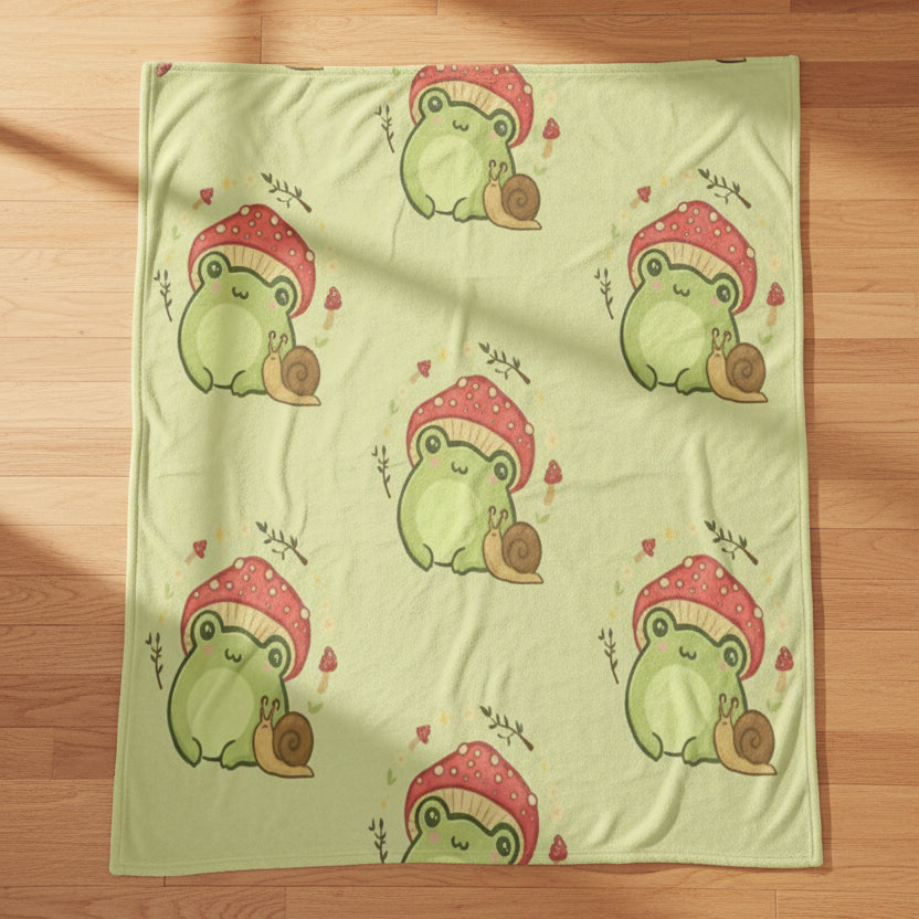 a light sage green blanket featuring a repeating pattern of cartoon green frogs wearing red mushrooms and snails, against a plain white background.