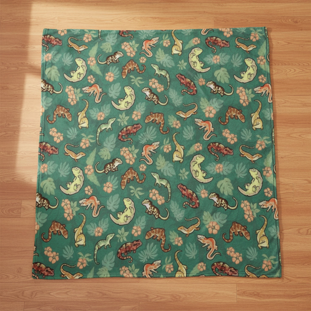 a blanket with a teal background and a pattern of New Caledonian geckos and tropical flowers