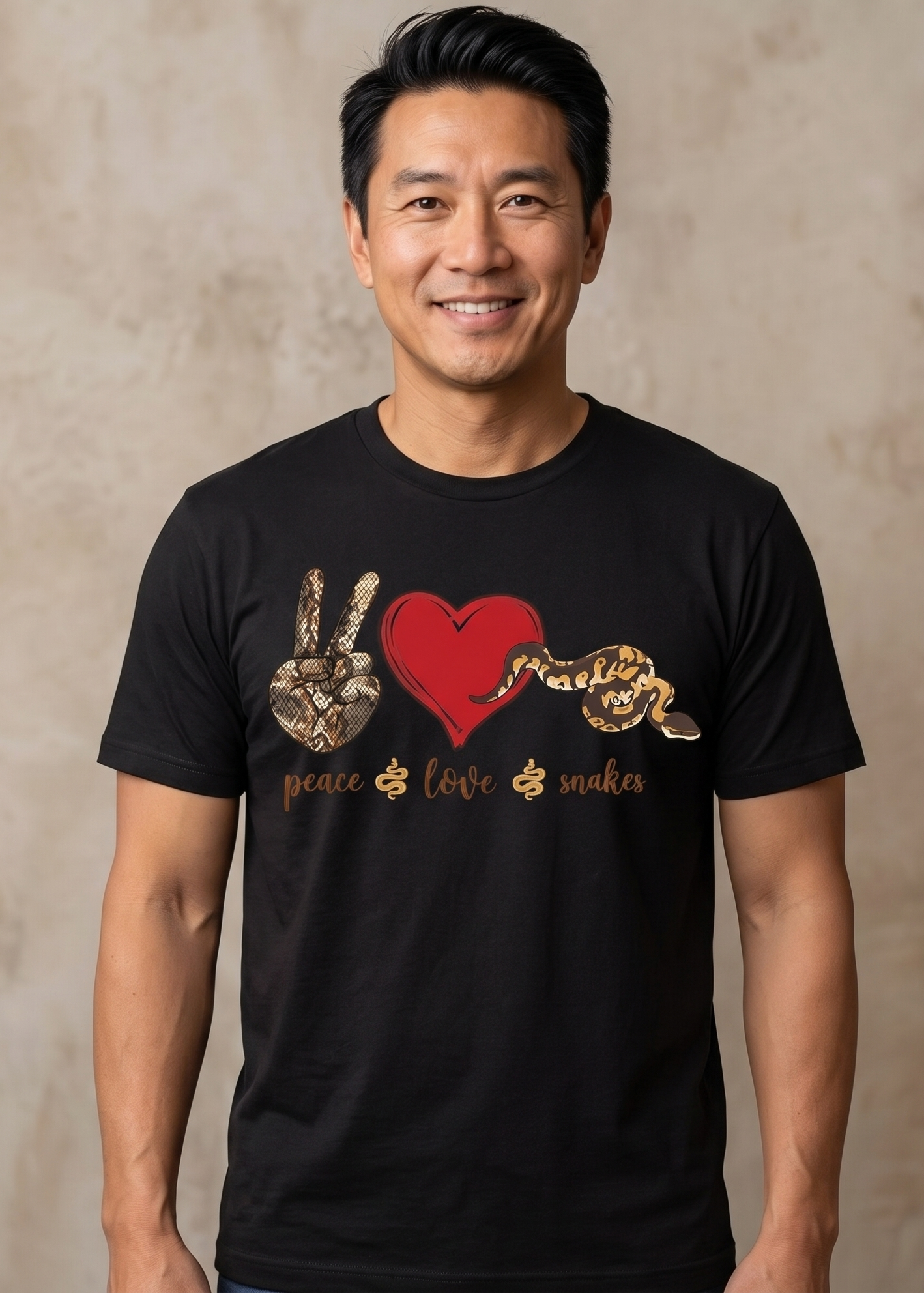 A smiling man wearing a black short-sleeve t-shirt with a graphic print featuring a red heart, a peace sign hand, a snake, and the words 'peace love snakes'.