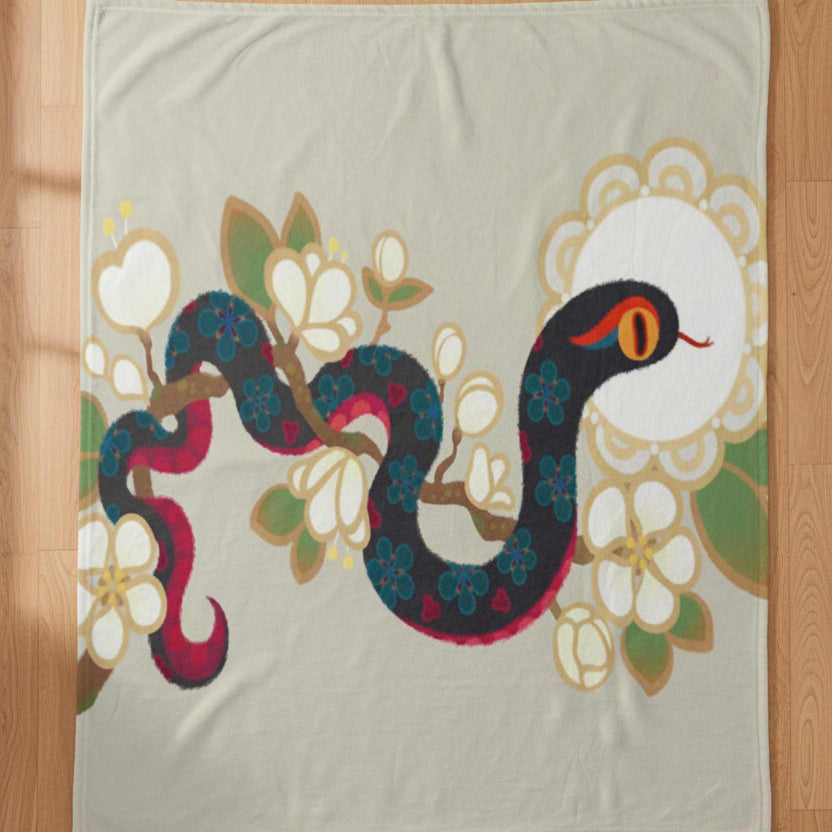 light beige blanket featuring a stylized snake wrapped through white flowers with green and gold leaves, against a plain white background.